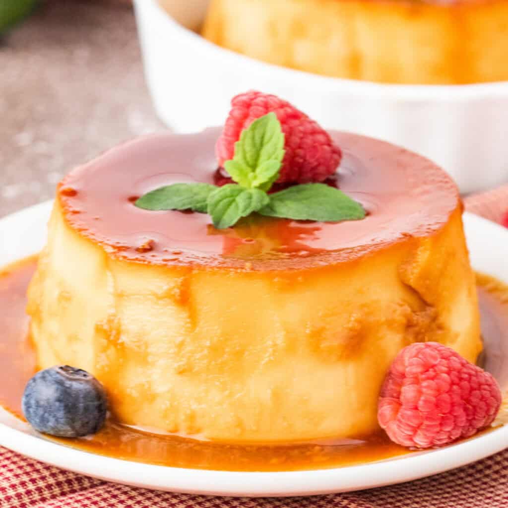 Close-up of mini caramel flan with caramel sauce, garnished with raspberry, mint, and a blueberry.
