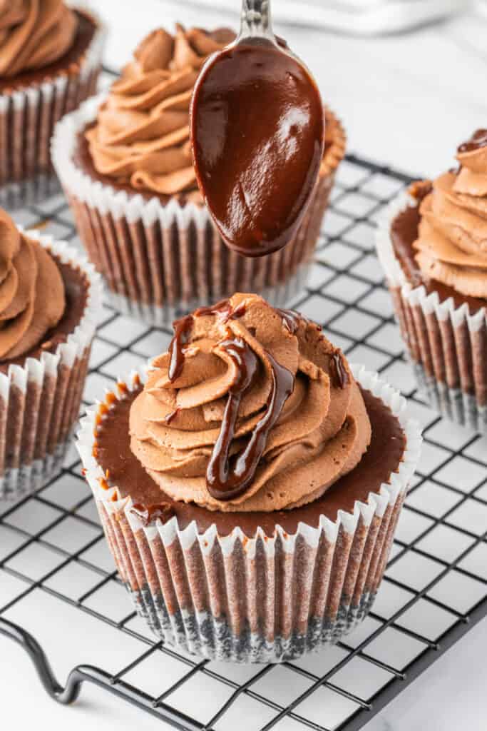 Spoon drizzling ganache over mini chocolate cheesecakes with piped frosting