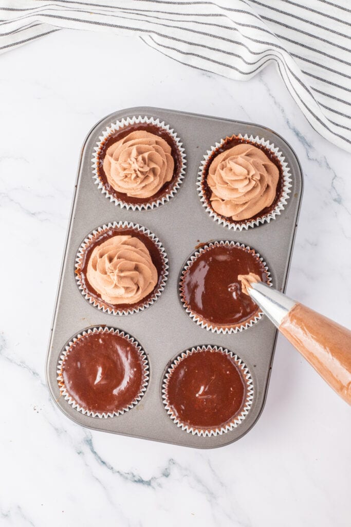 Piping chocolate whipped cream over mini chocolate cheesecakes in a muffin pan