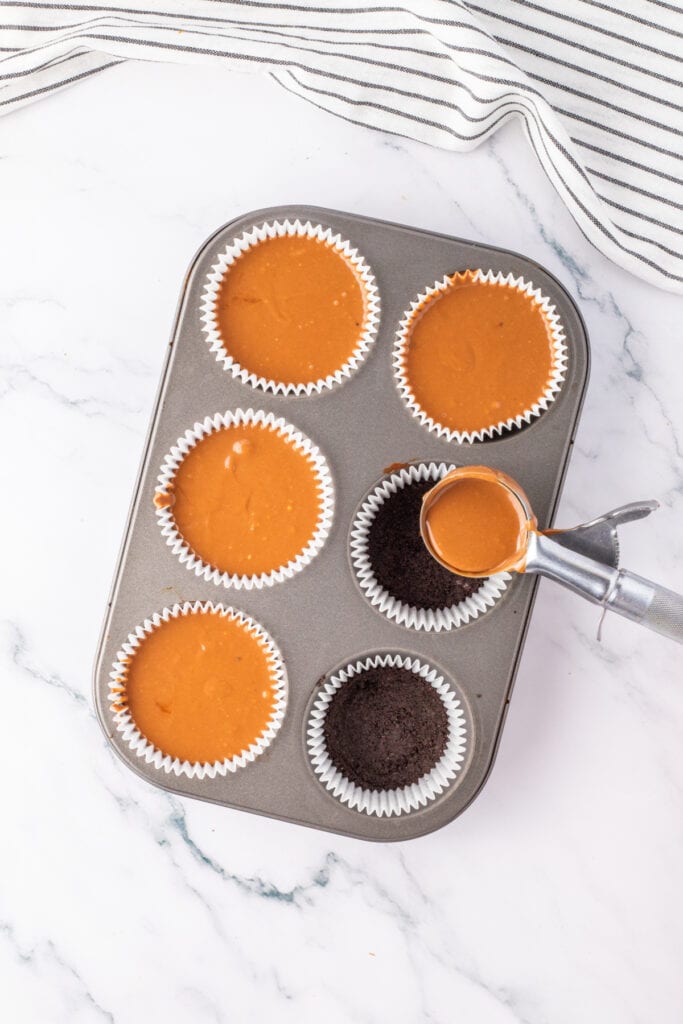 Filling liners with cheesecake batter and Oreo crust in a muffin tin using an ice cream scoop