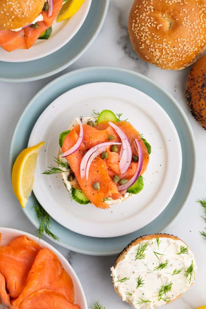 Open-faced smoked salmon bagel fully topped with cucumber, onion, capers, dill, and lemon wedge garnish.