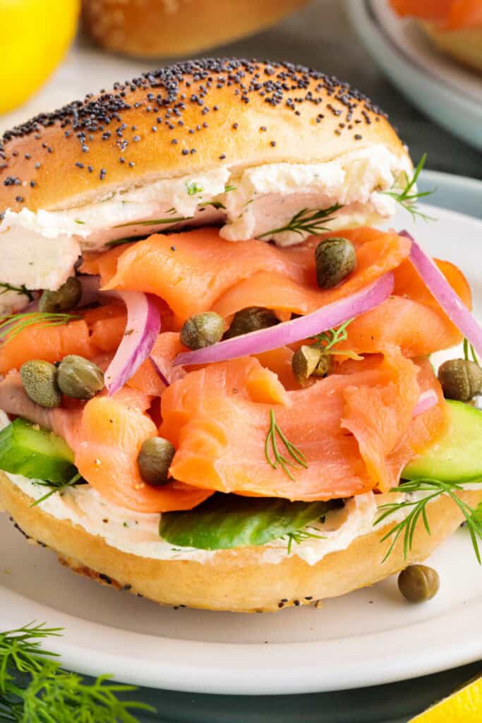 Close-up of a poppyseed bagel filled with cream cheese, smoked salmon, capers, cucumber, and red onion.
