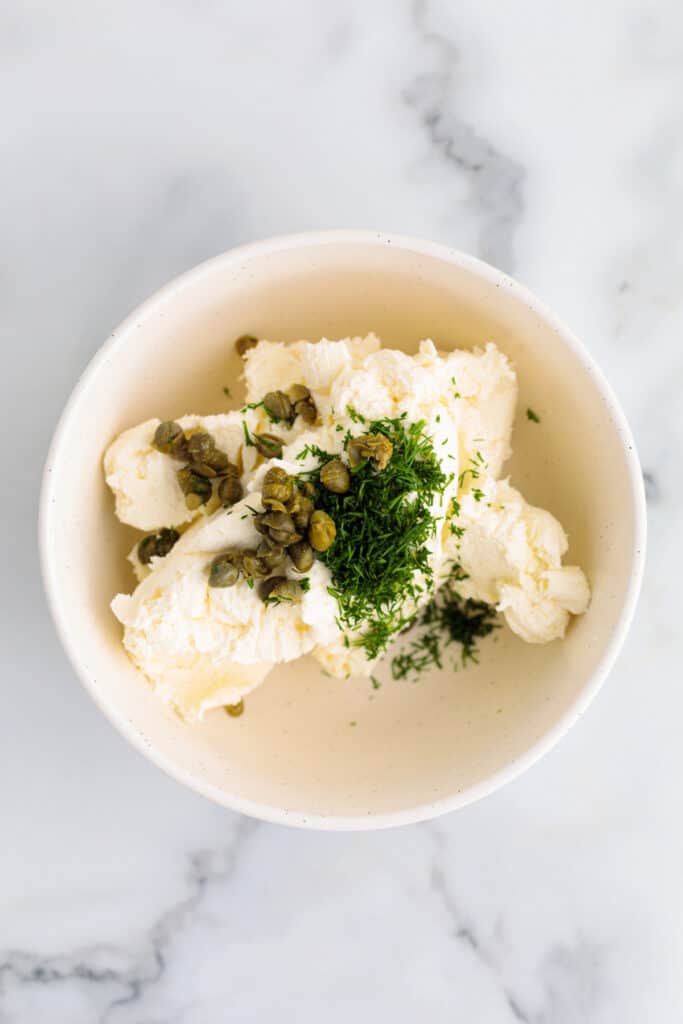 Cream cheese in a bowl with capers and chopped dill before mixing.