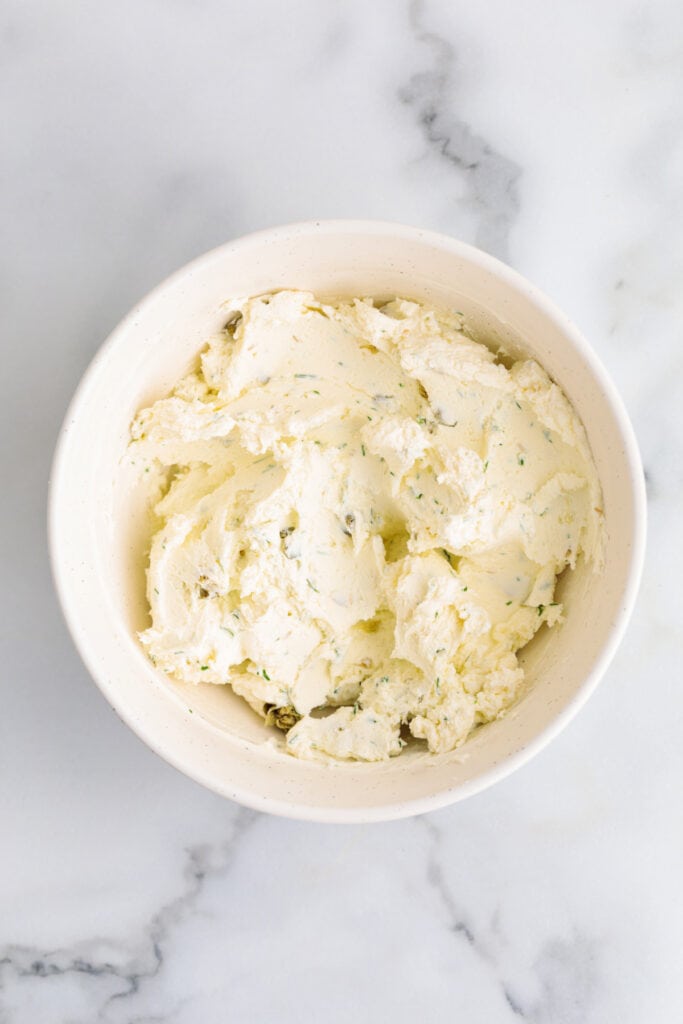 Dill and caper cream cheese mixture fully blended in a white bowl.