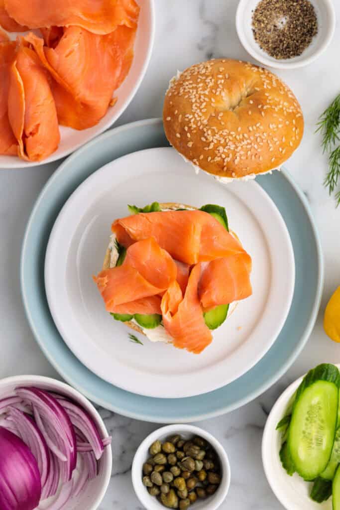 Cucumber-topped bagel with a generous portion of smoked salmon being layered on.