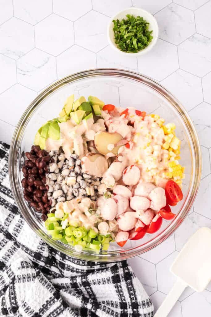 Southwest Potato Salad ingredients in a bowl with dressing poured over, ready to mix.