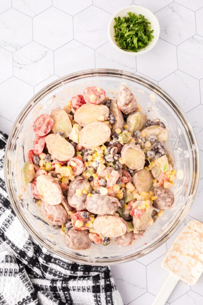 Mixed Southwest Potato Salad in a large glass bowl, coated in creamy dressing.