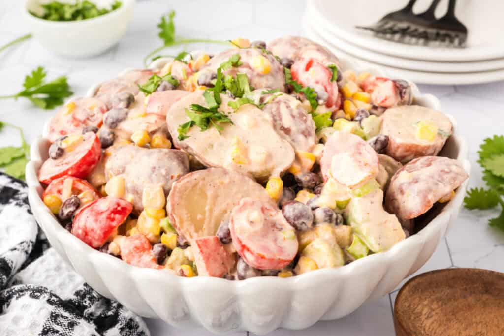 Side angle shot of Southwest Potato Salad served in a white bowl with fresh herbs.