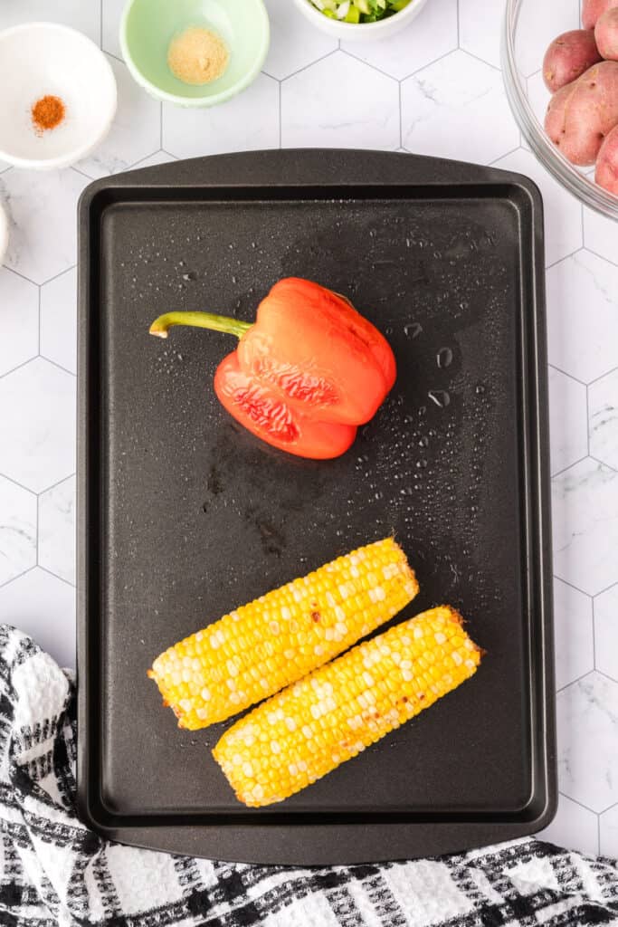 Roasted red bell pepper and charred corn on a black grill.