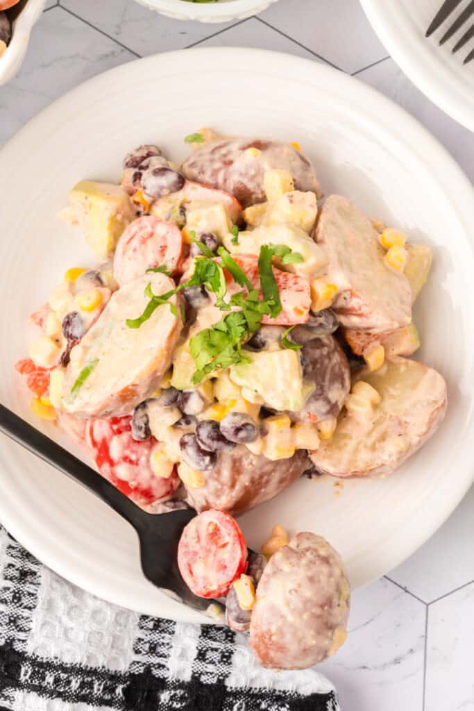 Close-up overhead of a plate of Southwest Potato Salad with a black fork, ready to eat.