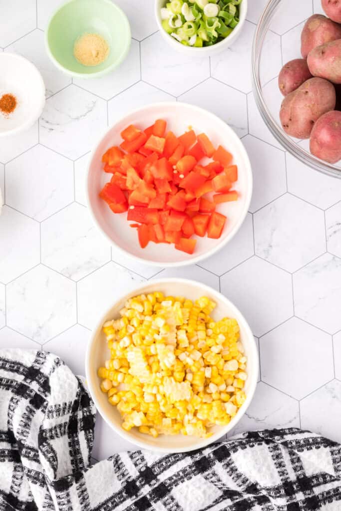 Bowls of chopped roasted red pepper and corn kernels displayed side by side.