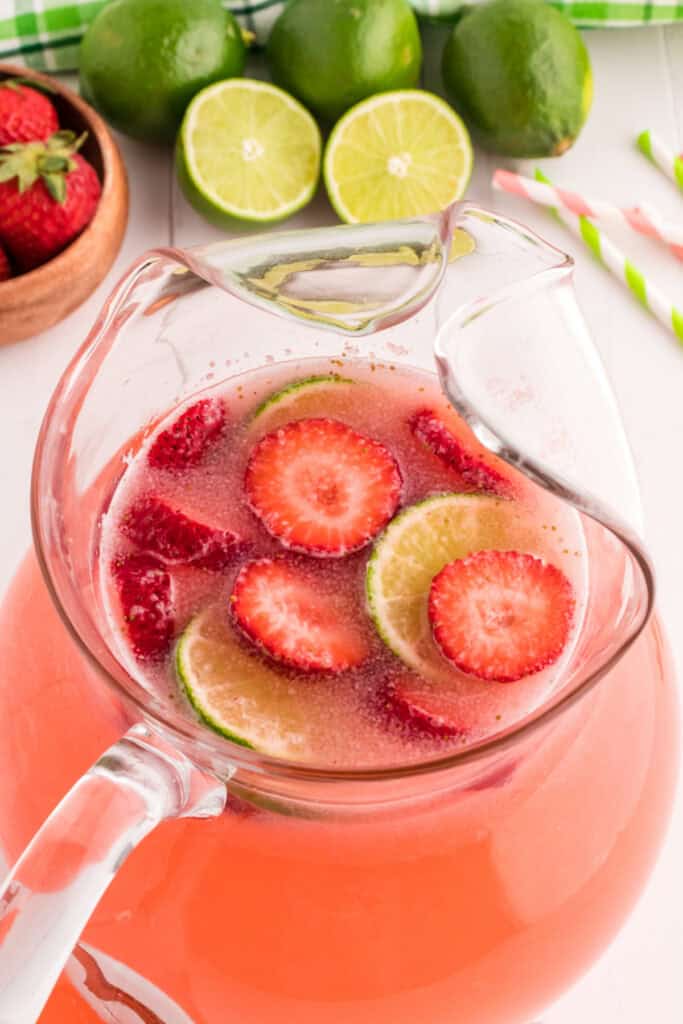 Close-up of the strawberry limeade pitcher with floating lime and strawberry slices, surrounded by fresh limes and strawberries.