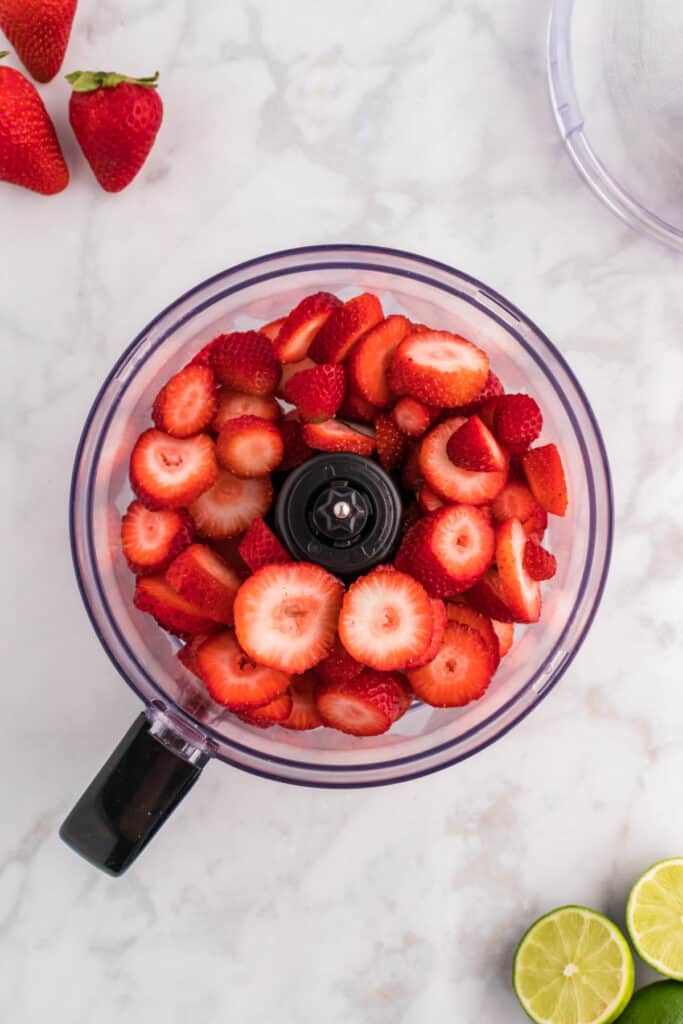 Fresh sliced strawberries placed inside a food processor, ready for blending.