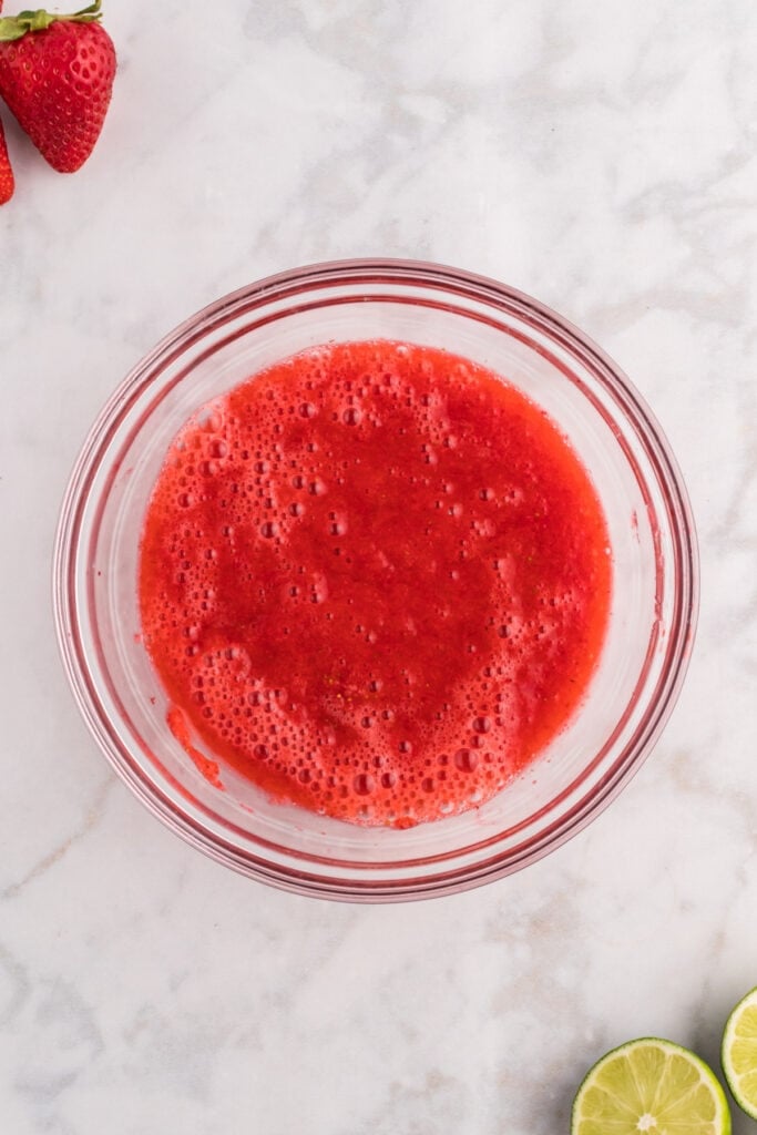 Smooth, strained strawberry purée collected in a clear glass bowl.