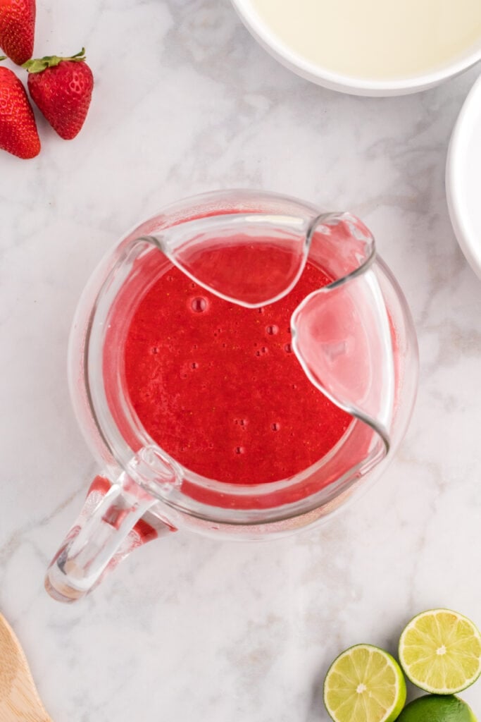 Strawberry purée added to the lime juice mixture in a glass pitcher.