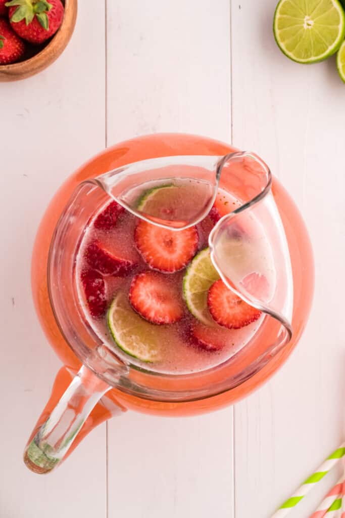 Strawberry limeade garnished with fresh lime and strawberry slices in a glass pitcher.