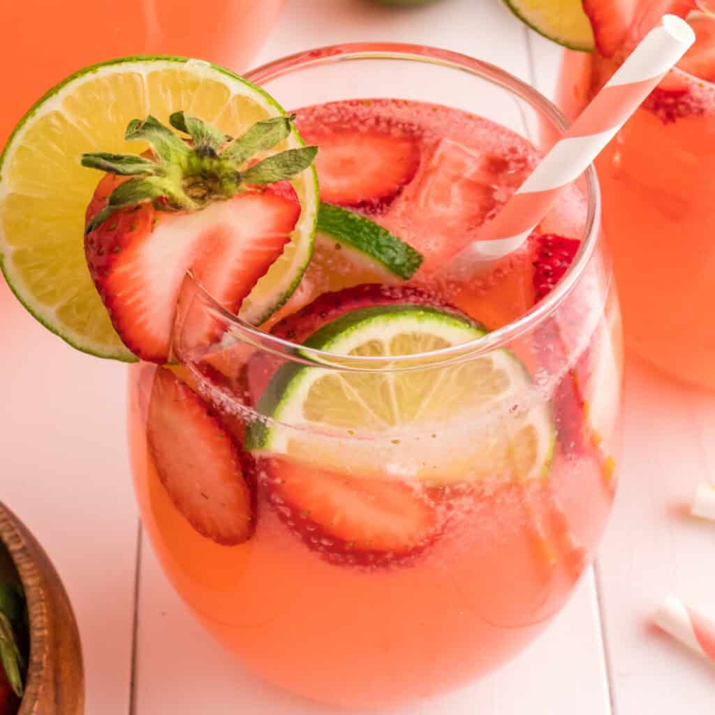 Close-up square image of a strawberry limeade glass with lime and strawberry slices and a pink striped straw, perfect for social sharing.