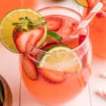 Close-up square image of a strawberry limeade glass with lime and strawberry slices and a pink striped straw, perfect for social sharing.