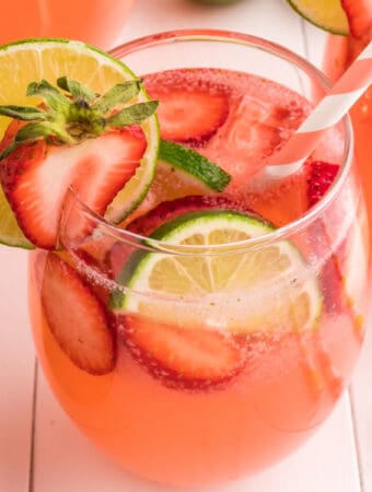 Close-up square image of a strawberry limeade glass with lime and strawberry slices and a pink striped straw, perfect for social sharing.