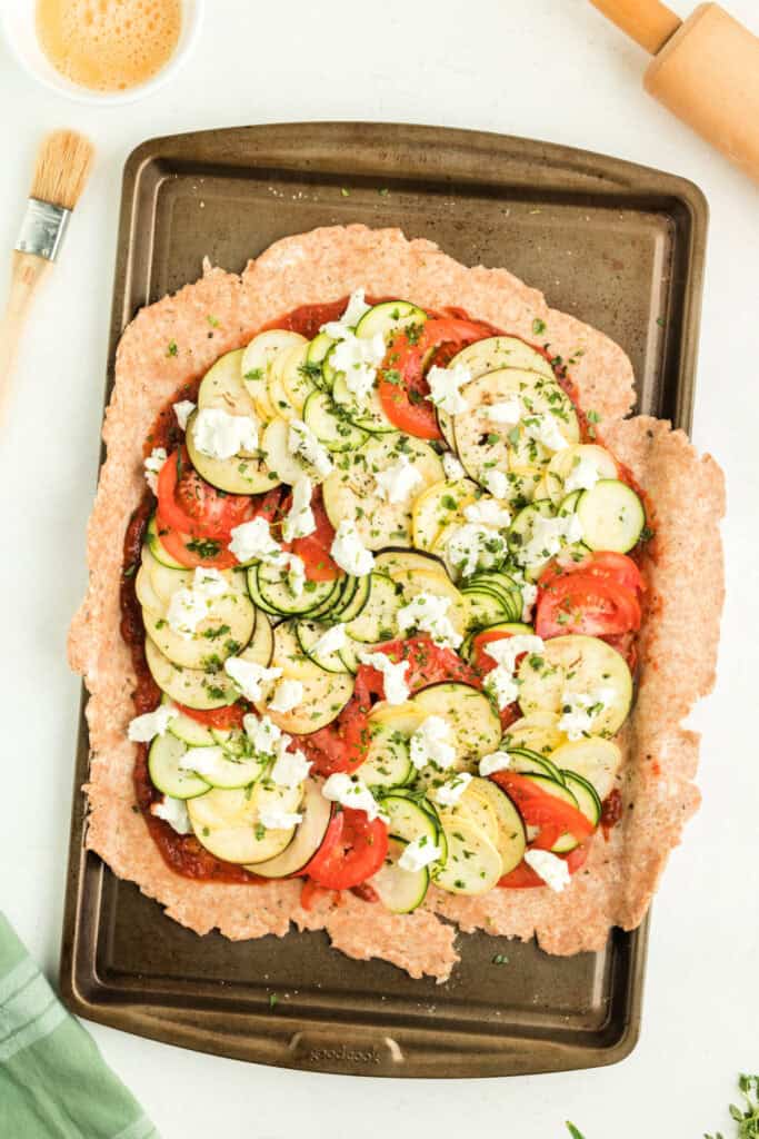 Galette before baking, topped with fresh herbs and goat cheese, edges of crust unfolded.