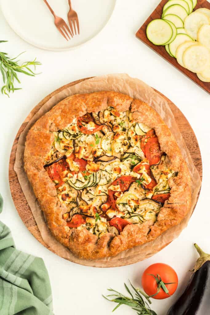 Fully baked summer vegetable galette on a wooden board with golden brown crust and colorful filling.