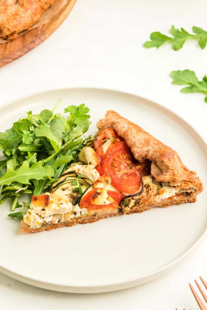 Plated slice of vegetable galette served with fresh green salad on a white plate.