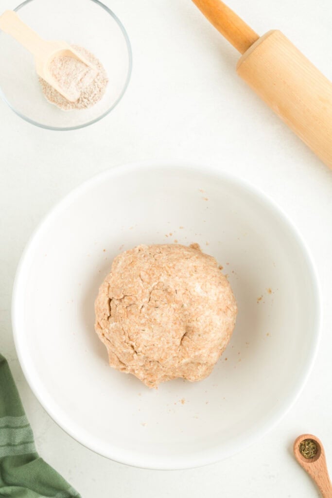 Whole wheat galette dough formed into a ball and resting in a white bowl.