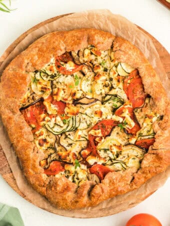 Overhead view of summer vegetable galette on parchment-lined wooden board, ready to serve.
