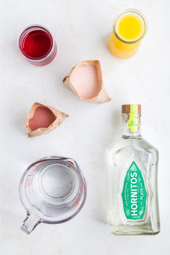Ingredients for tequila sunrise jello shots laid out, including tequila, jello powder, grenadine, and orange juice.