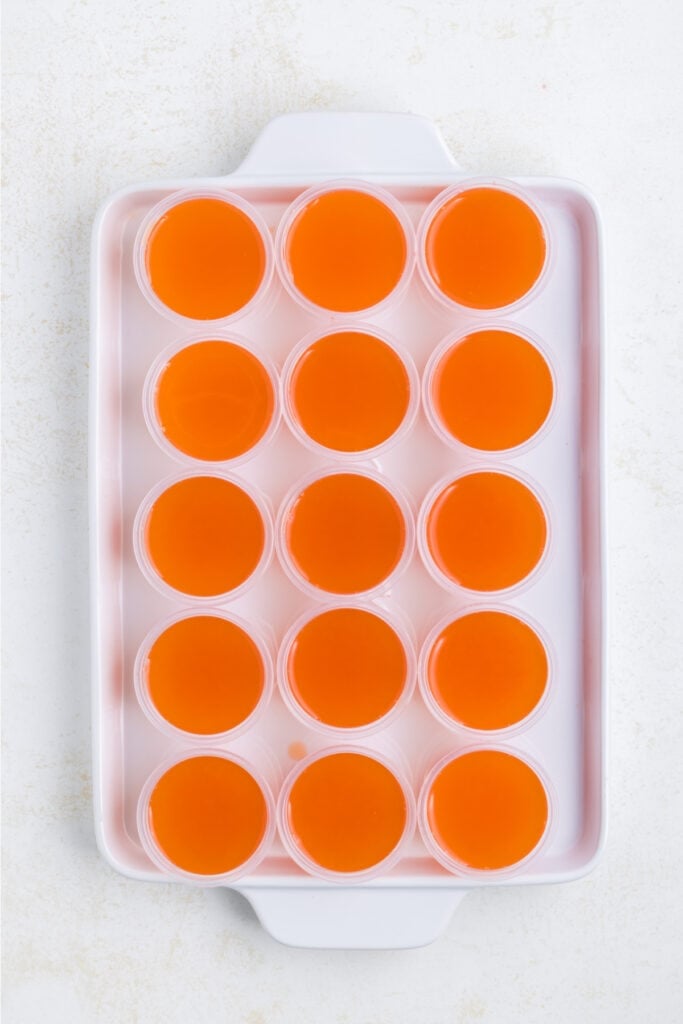Tray of shot cups filled with vibrant orange jello mixture.