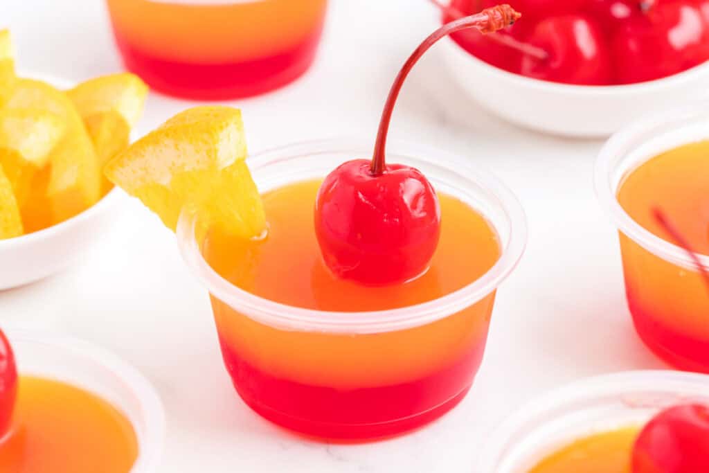 Finished tequila sunrise jello shot garnished with maraschino cherry and orange slice.
