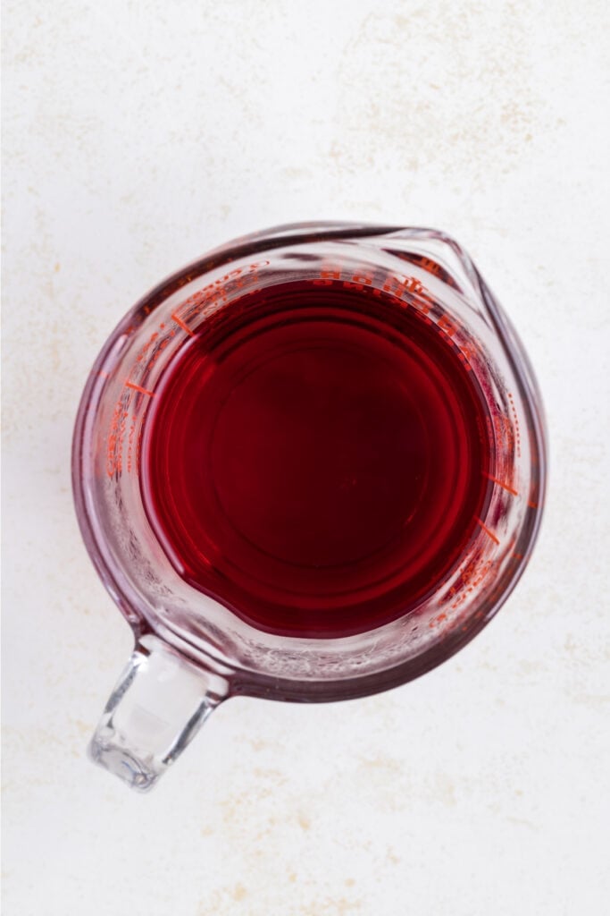 Measuring cup filled with red liquid, prepared cherry jello mixture for jello shots.