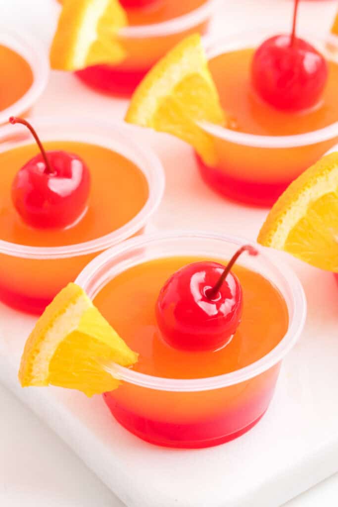 Tray of tequila sunrise jello shots garnished with cherries and orange wedges.