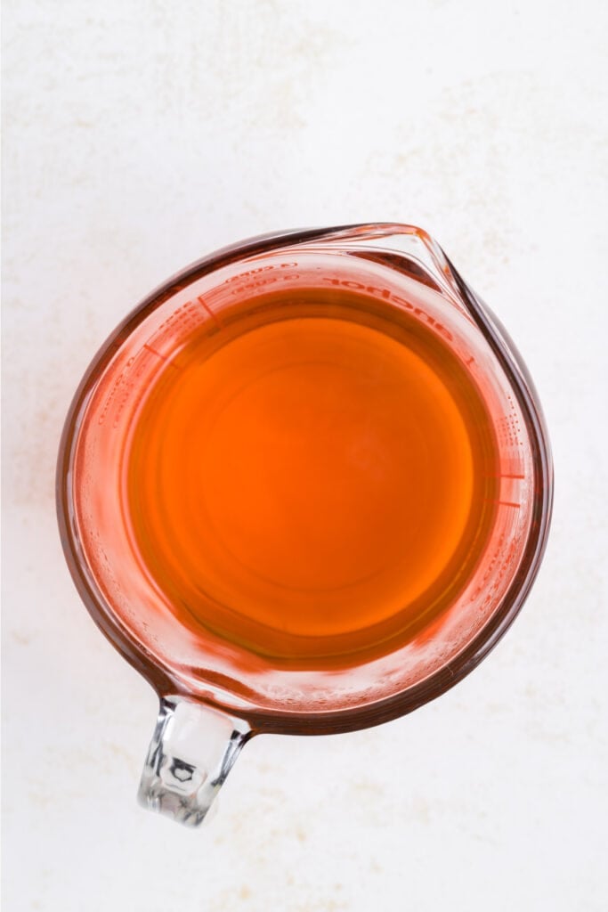 Measuring cup filled with prepared orange jello mixture.