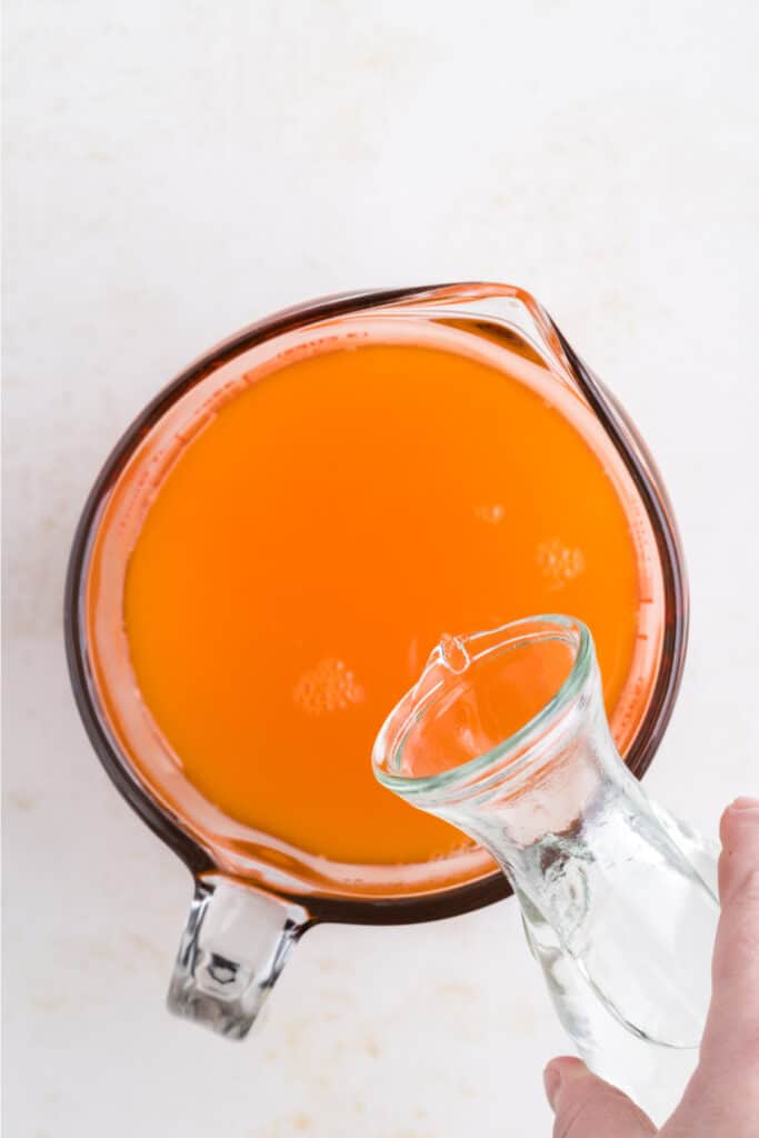 Tequila being added to prepared orange jello mixture in a measuring cup.