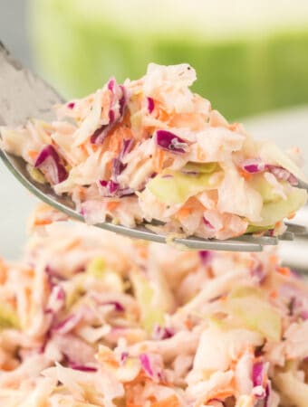 Square close-up of a forkful of creamy coleslaw lifted above a full bowl of salad.
