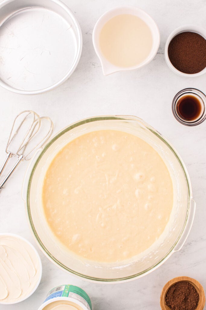 Mixed cake batter in a glass bowl surrounded by ingredients.