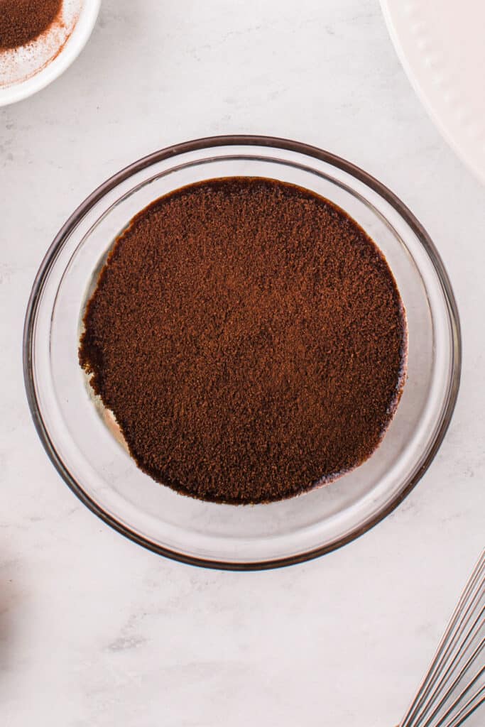 Bowl of espresso syrup with coffee powder floating on top.
