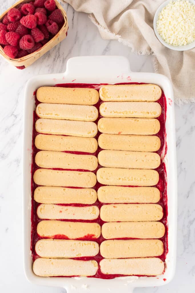 Second layer of ladyfingers arranged neatly over the raspberry layer in the baking dish.