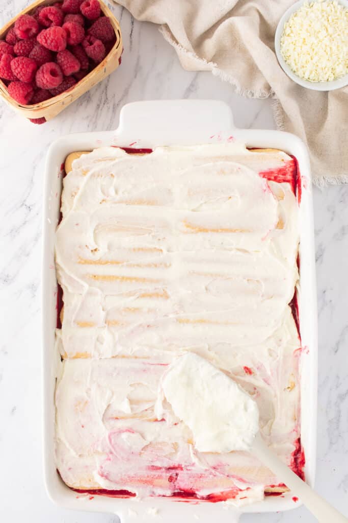 Second layer of mascarpone cream being spread smoothly over the ladyfingers using a spatula.