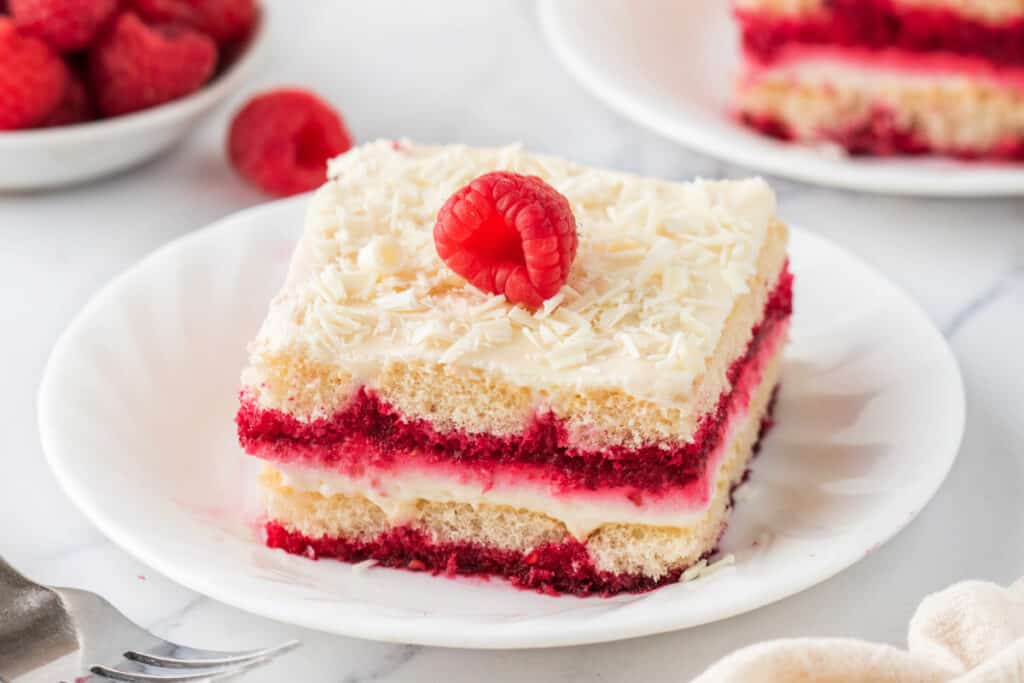 Slice of tiramisu garnished with a fresh raspberry on top, served on a white plate.