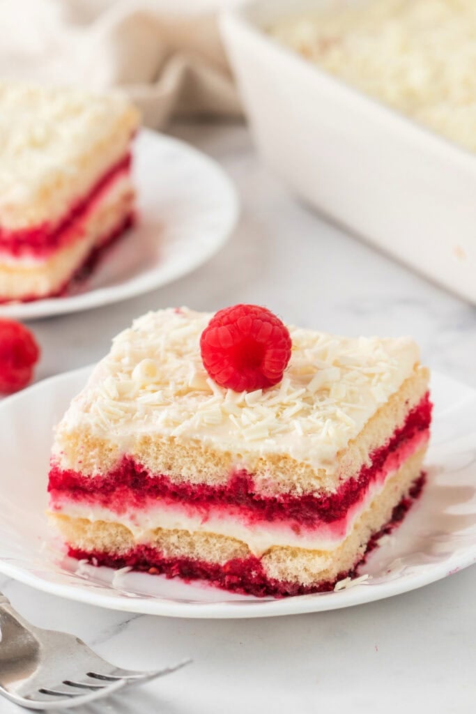 Two slices of White Chocolate Raspberry Tiramisu on plates, garnished with fresh raspberries.