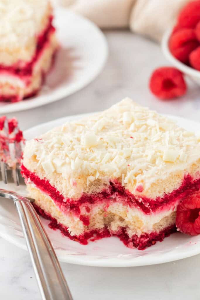 Partially eaten slice of tiramisu showing creamy mascarpone and vibrant raspberry layers.