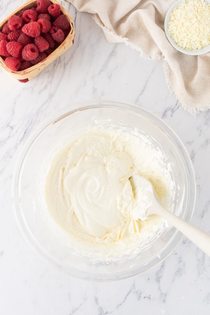 Melted white chocolate being folded into mascarpone cream mixture with a spatula.