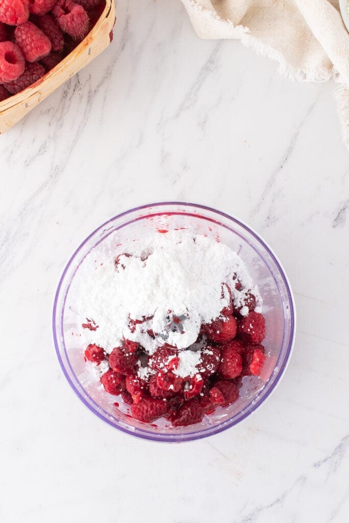 Food processor filled with raspberries and powdered sugar ready to be blended for the raspberry layer.