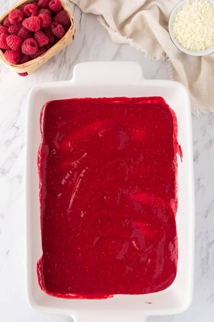 White baking dish with the first layer of raspberry sauce evenly spread out for tiramisu.