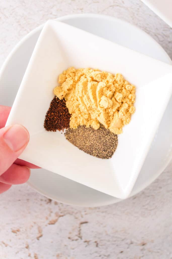 Close-up of a bowl of ground mustard, black pepper, and chili powder