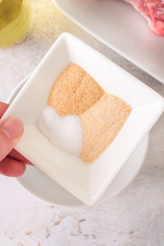 Bowl of garlic powder, onion powder, and salt being held over a plate