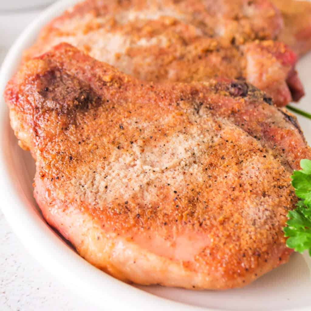 Close-up of juicy smoked pork chops with a crispy rub, served on a white plate with parsley garnish