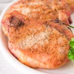 Close-up of juicy smoked pork chops with a crispy rub, served on a white plate with parsley garnish